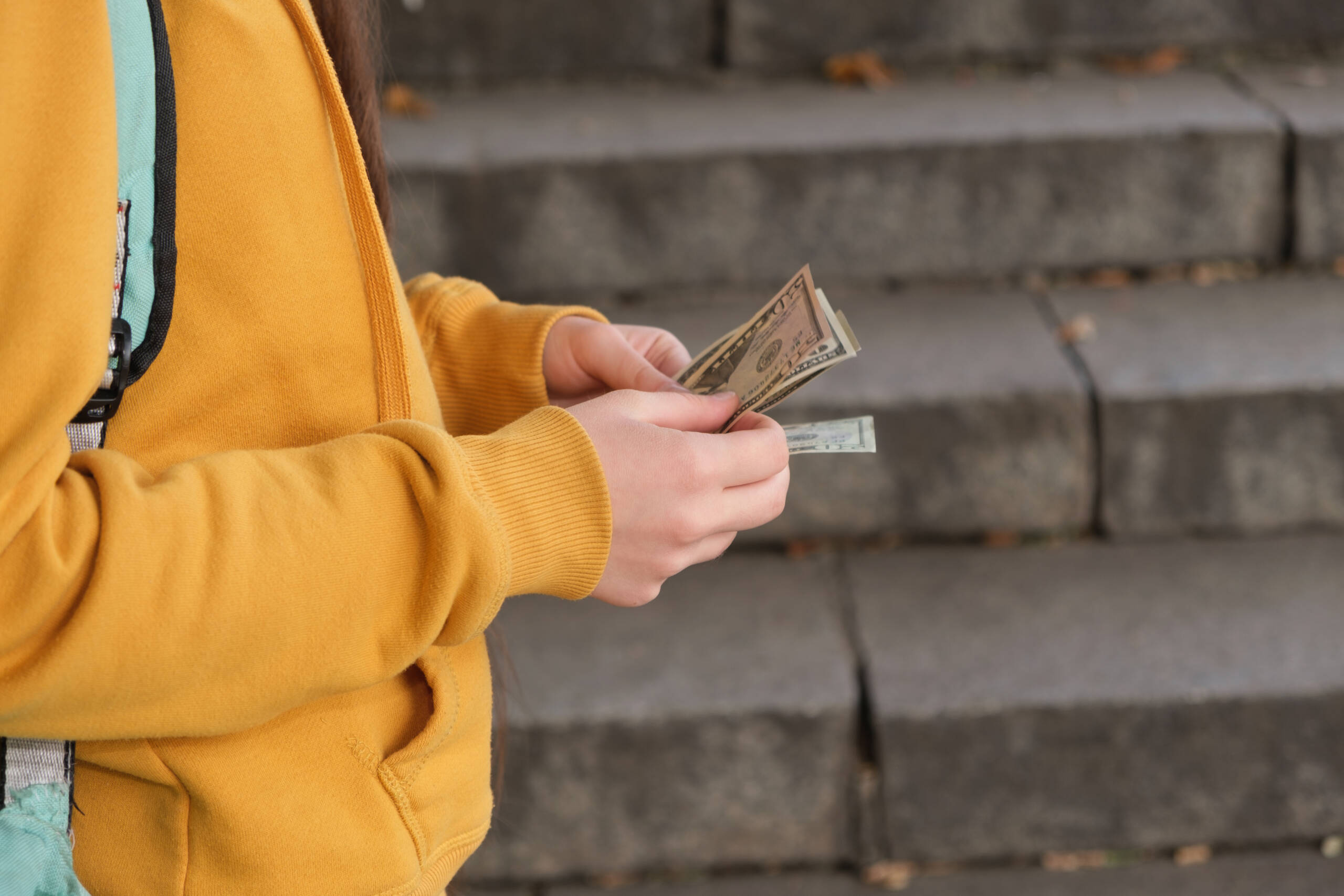 Teenage girl counts dollar bills on the background of the stairs counting money for finances